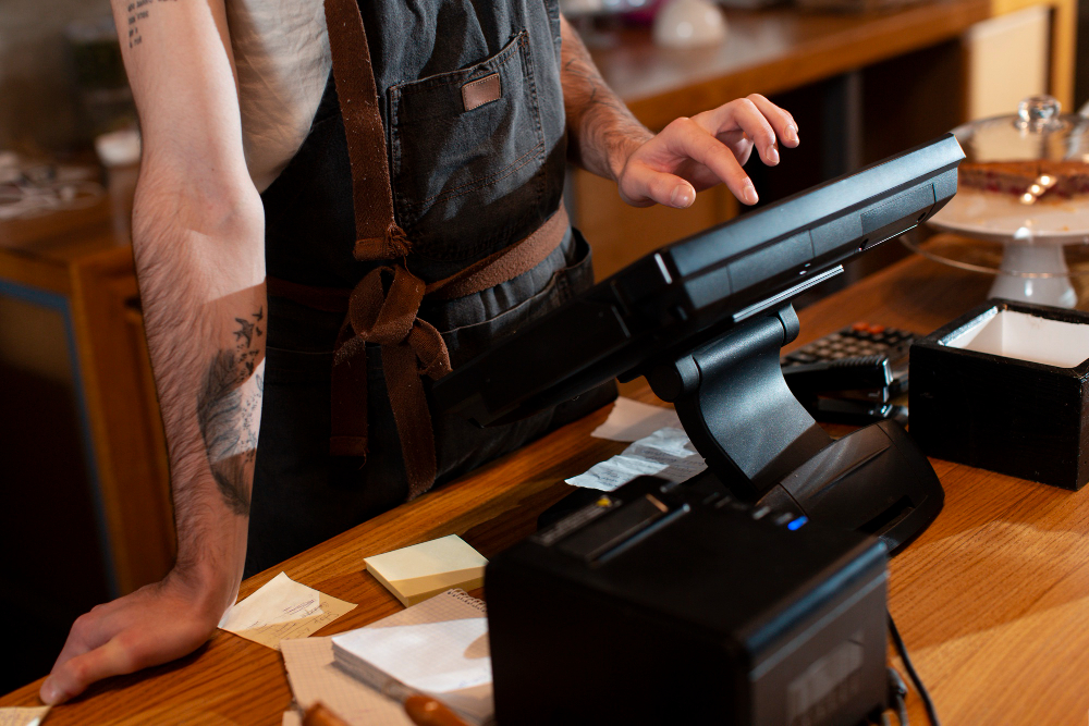 Staff member tapping a touchscreen POS terminal beside a receipt printer at a restaurant counter