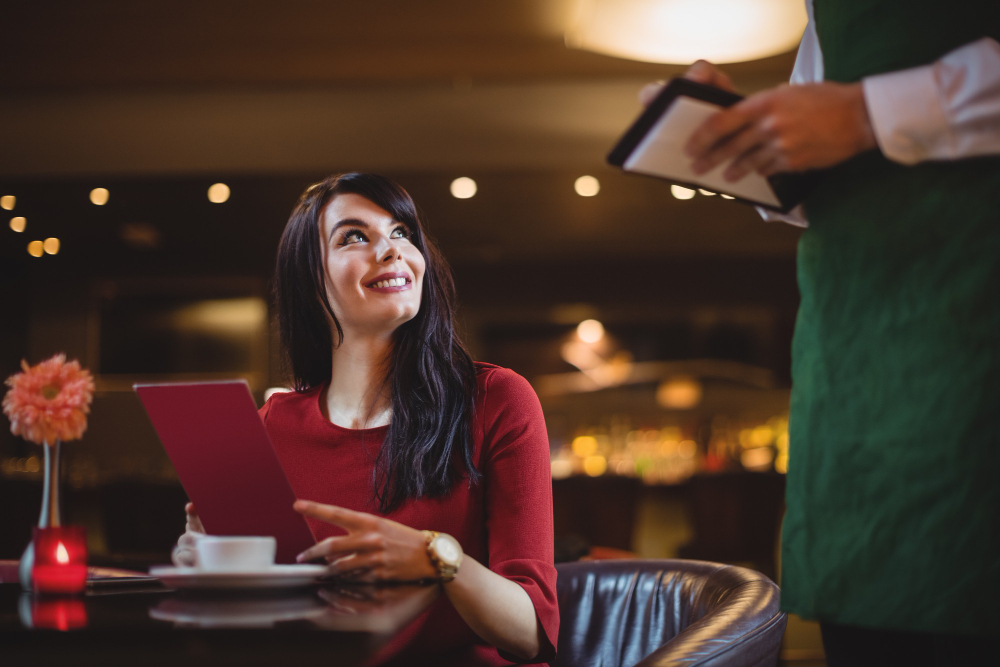 Guest at a dining table smiling at a server who is taking her order on a tablet